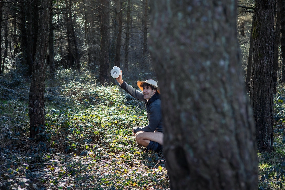 man squatting behind a tree, pooping in the woods, a necessary skill during a zombie apocalypse