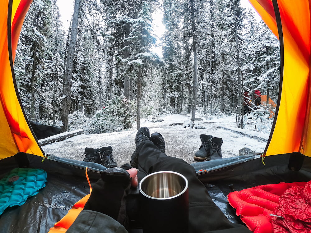 backpacker camping in snow, inside tent with mug of hot water