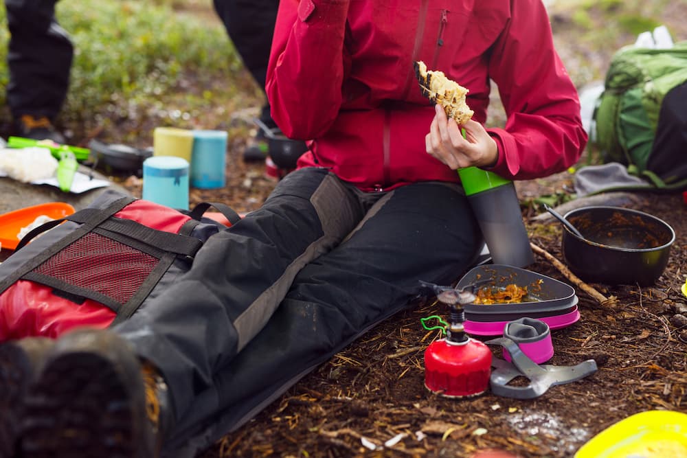 backpacker sitting on ground eating meal at campsite