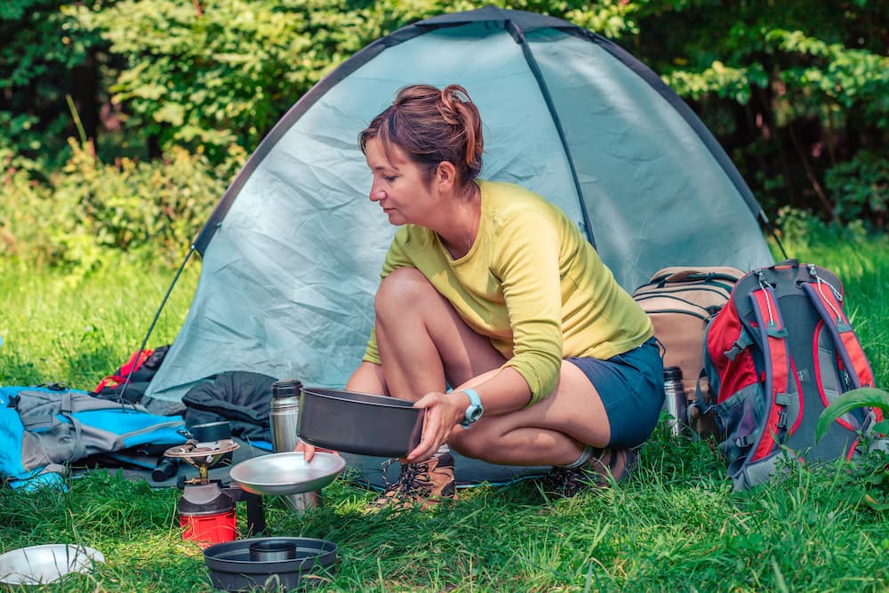 woman backpacker setting up campsite with tent and stove